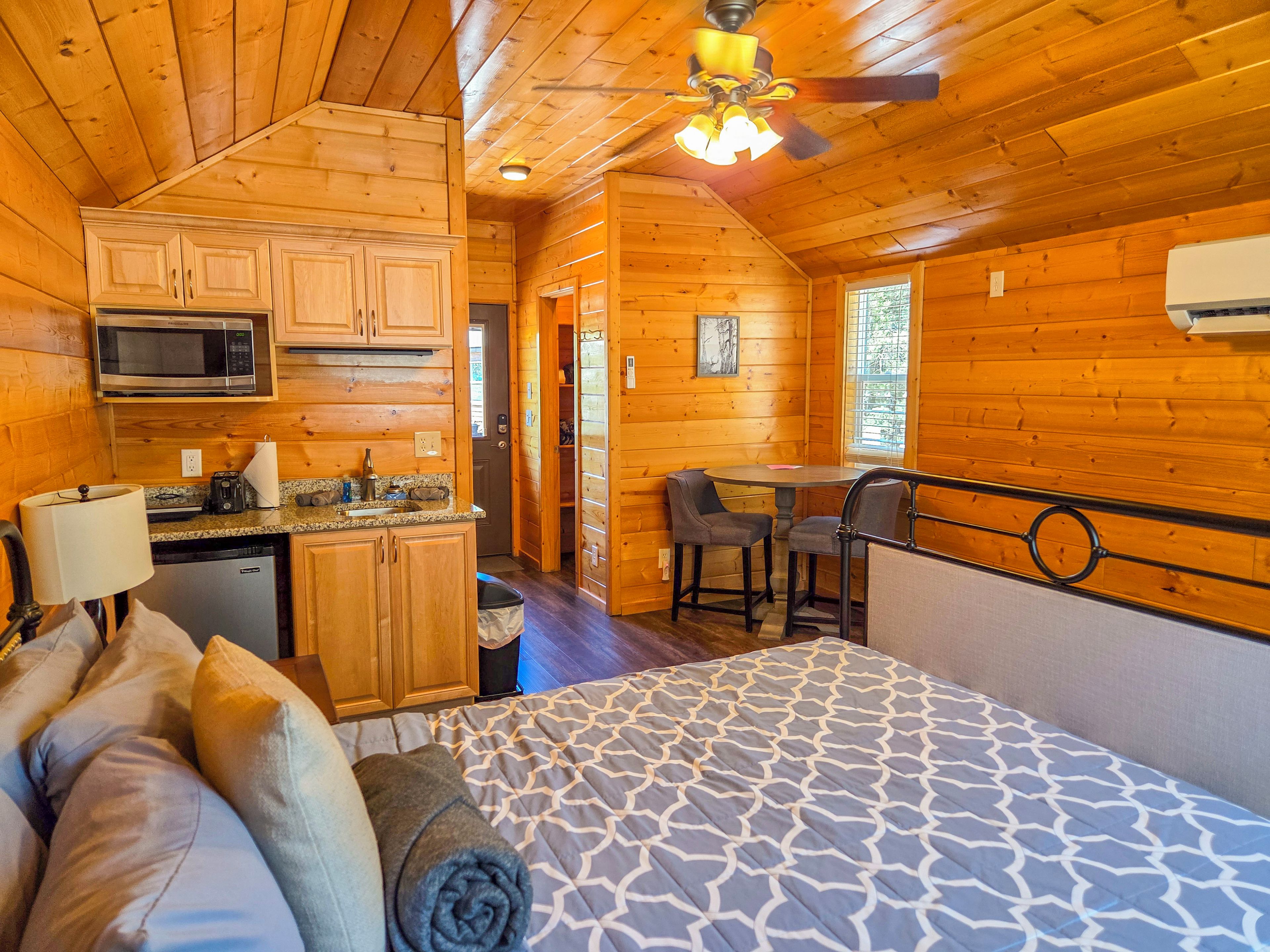 A log cabin with a kitchenette, a dining area, and a bed with a patterned bedspread.