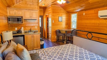 A log cabin with a kitchenette, a dining area, and a bed with a patterned bedspread.