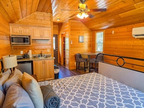 A log cabin with a kitchenette, a dining area, and a bed with a patterned bedspread.