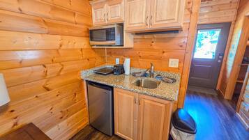 A compact kitchen with wooden cabinetry, a microwave, a sink, and a dishwasher.