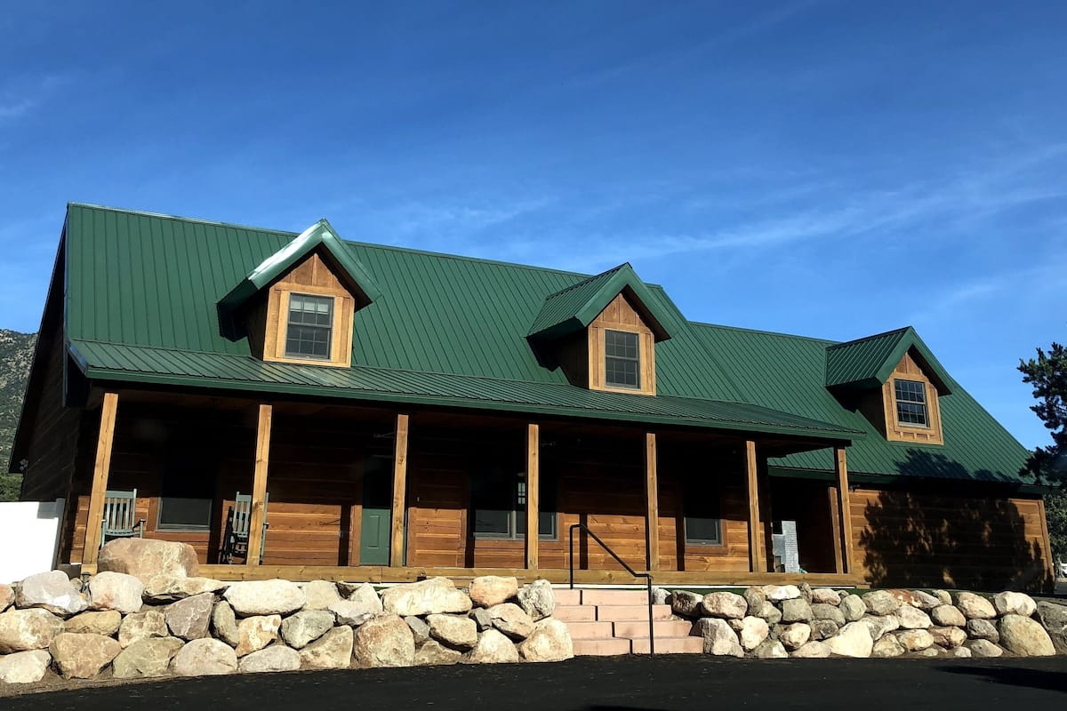 A log cabin with a green metal roof, wooden exterior, and a stone foundation.
