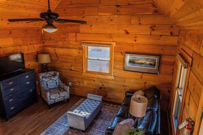 A log cabin interior with a ceiling fan, a television, a patterned armchair, a cushioned bench, a sofa, and a framed picture on the wall. - Holmstead Ranch Resort (Veyo)