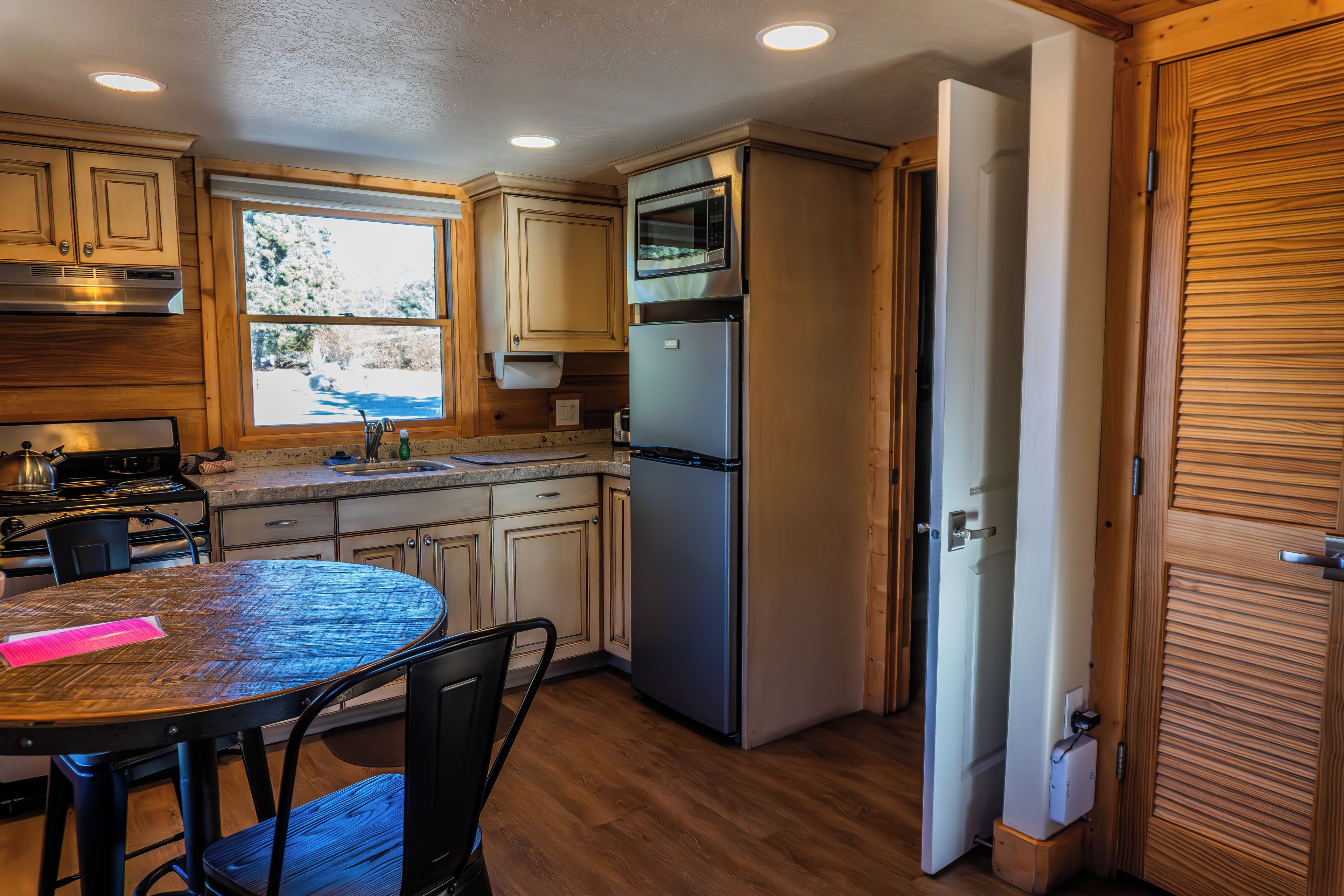 A compact kitchen with wooden cabinets, a stainless steel refrigerator, a microwave, and a stove.