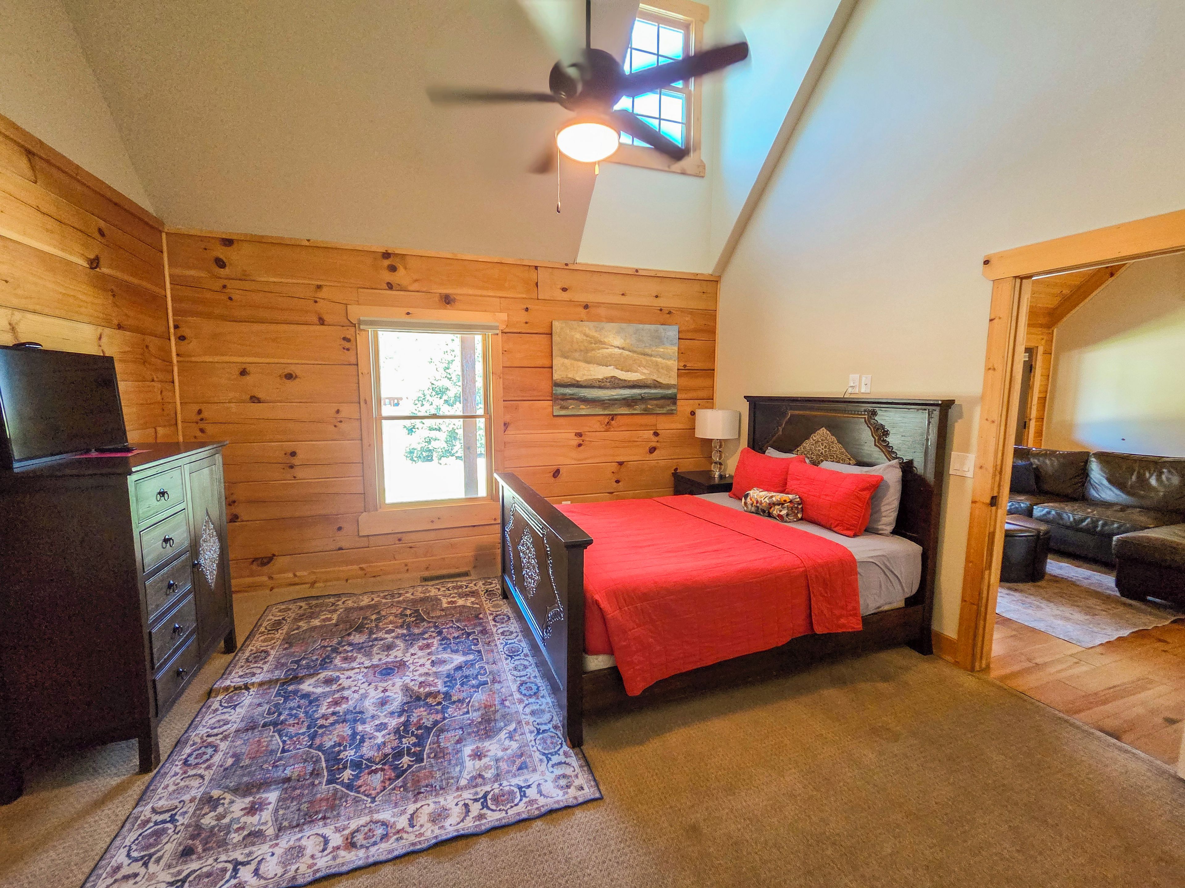 Une chambre à coucher avec un lit, une commode, un tapis, un ventilateur de plafond et une fenêtre.