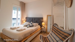 Una habitación de hotel con una cama, una silla, una mesita, una lámpara y un espejo.