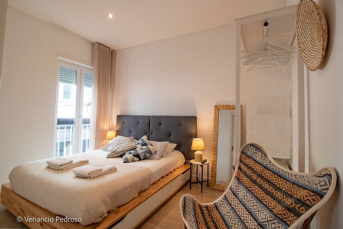 Una habitación de hotel con una cama, una silla, una mesita, una lámpara y un espejo.