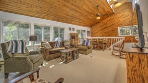 Ein geräumiges Wohnzimmer mit Holzbalken an der Decke, großen Fenstern und einer gemütlichen Sitzecke mit Sofas und einem Couchtisch.