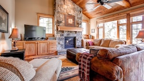A cozy living room with a stone fireplace, wooden ceiling, and large windows. - Christie Heights Retreat (Breckenridge)