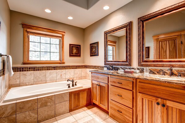 A bathroom with a large bathtub, wooden vanity, and two mirrors.