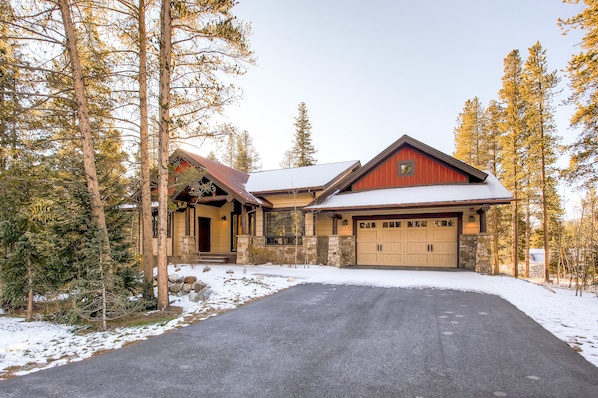 A two-story house with a garage, surrounded by tall trees and a snow-covered driveway.
