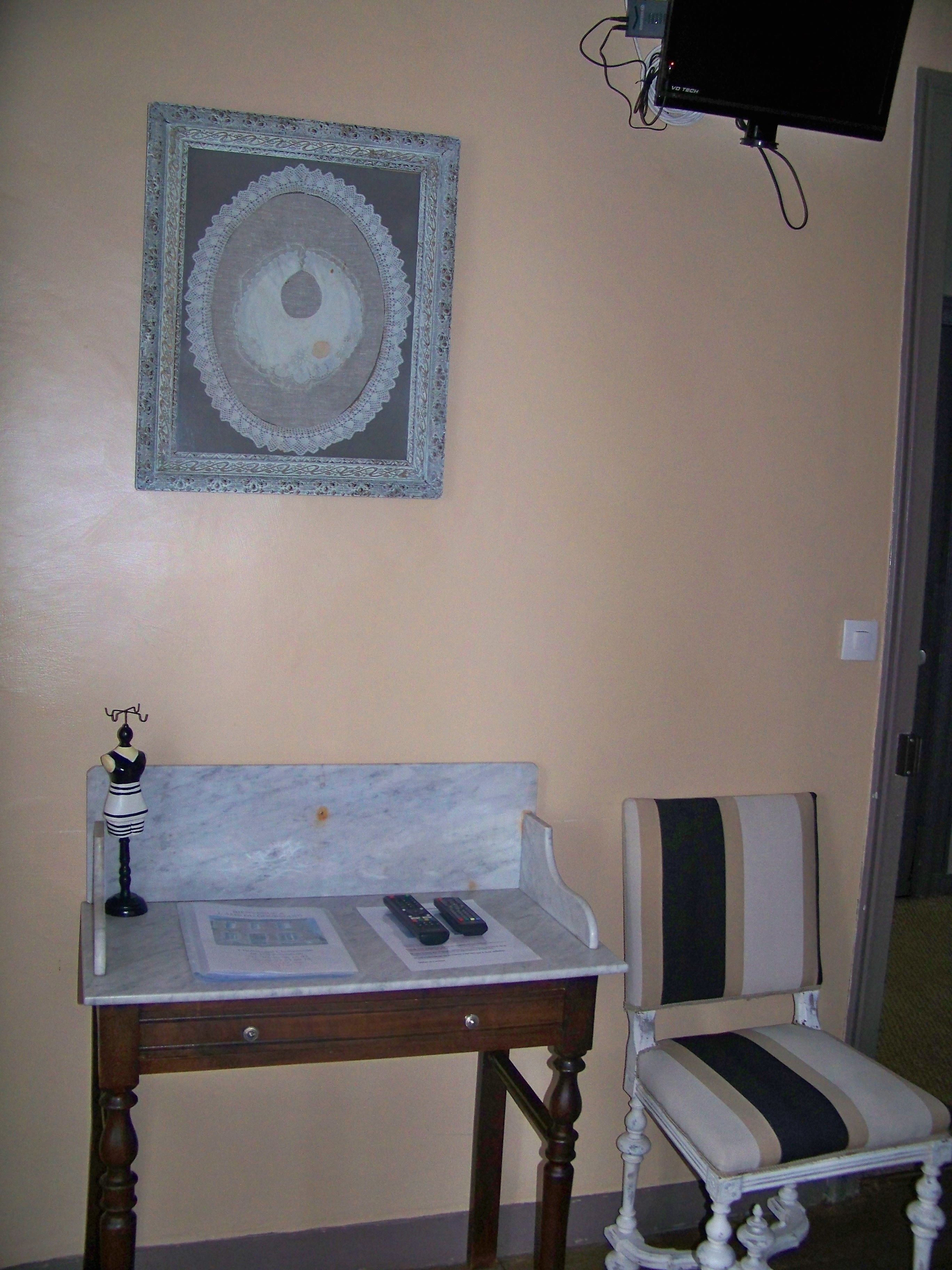 A room with a marble table, a decorative chair, a television mounted on the wall, and a framed artwork above the table.