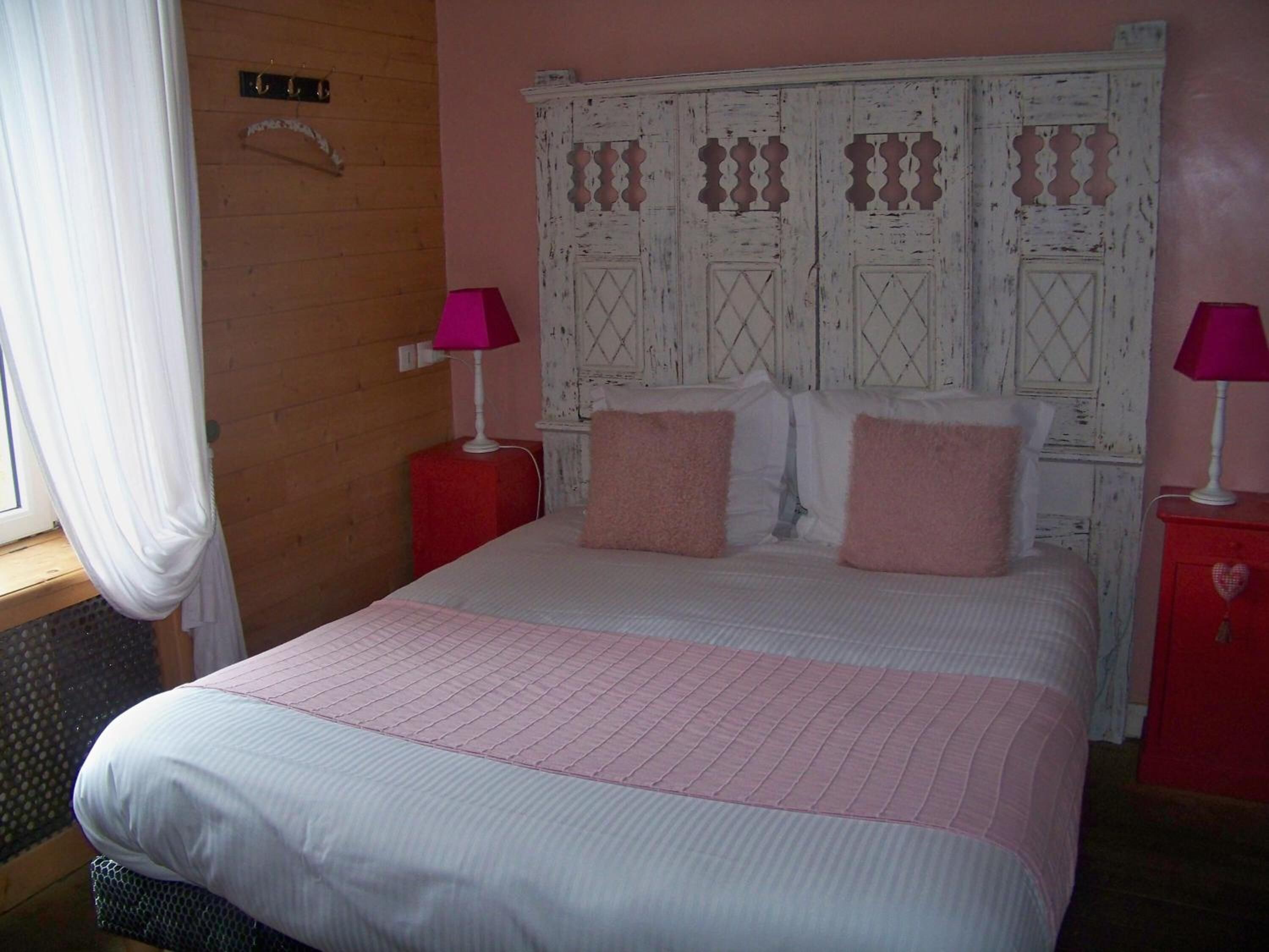 A bedroom with a large bed, two bedside tables, a wooden headboard, and a window with curtains.
