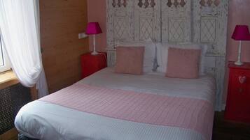 A bedroom with a large bed, two bedside tables, a wooden headboard, and a window with curtains.