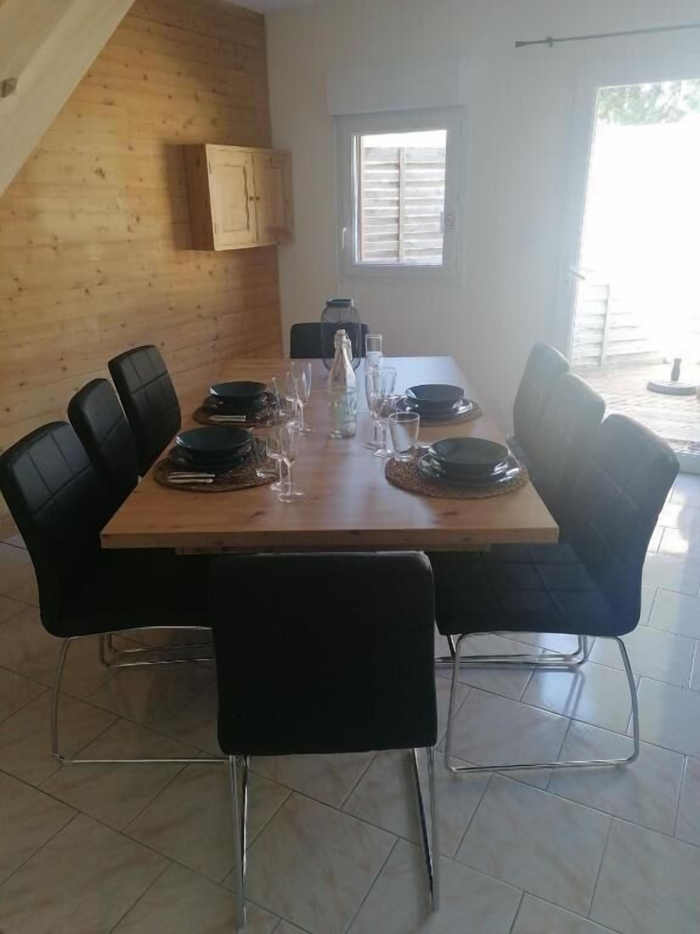 Un coin repas avec une table en bois dressée pour six personnes, entourée de chaises noires aux pieds chromés.
