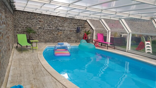 An indoor swimming pool with a stone wall, a glass ceiling, and colorful pool toys. - L'Âme Du Gourmand (Pontorson)