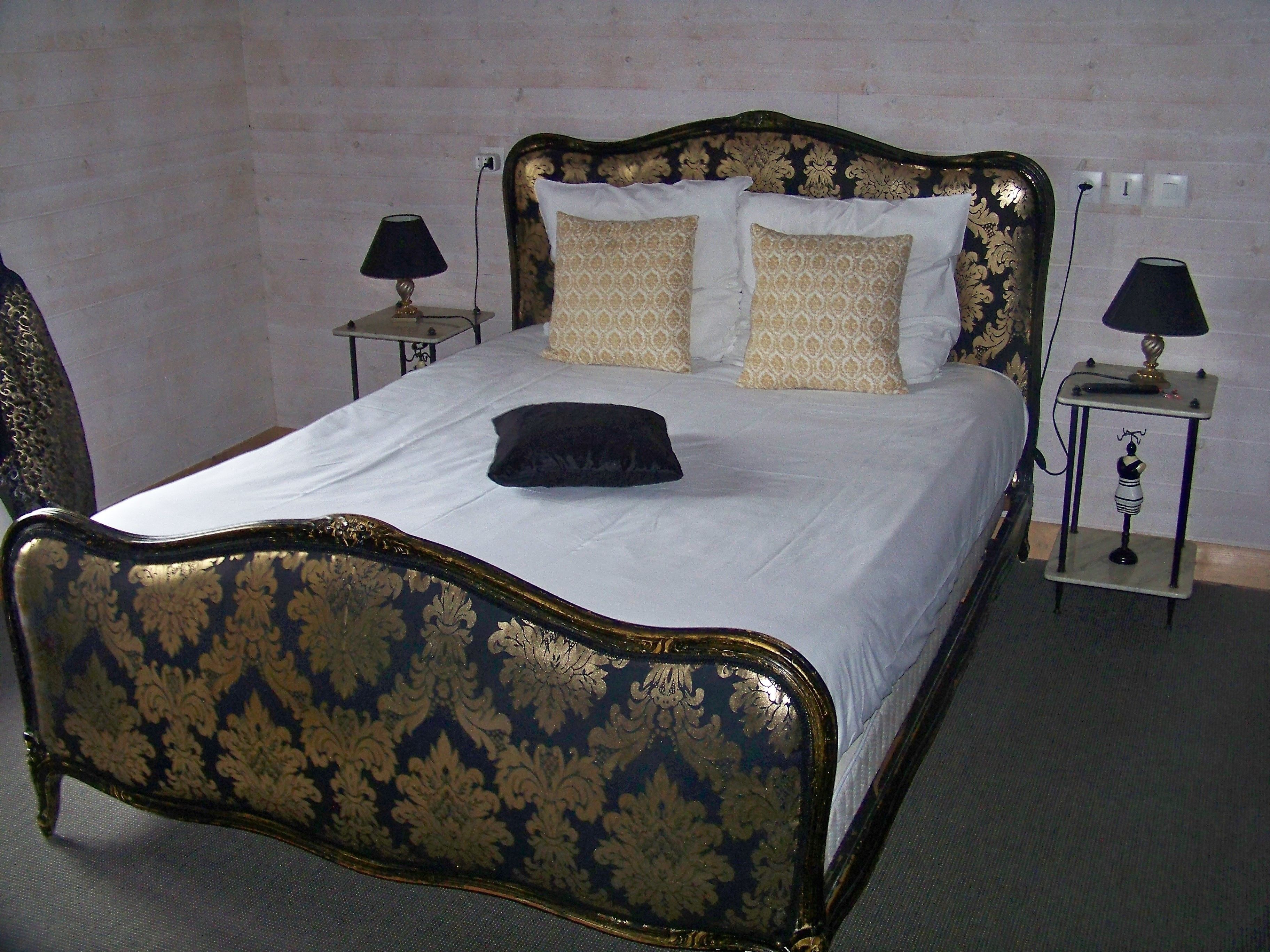 Un letto con una testiera e un bordo inferiore scuri e decorati, due comodini con lampade e cuscini a fantasia.