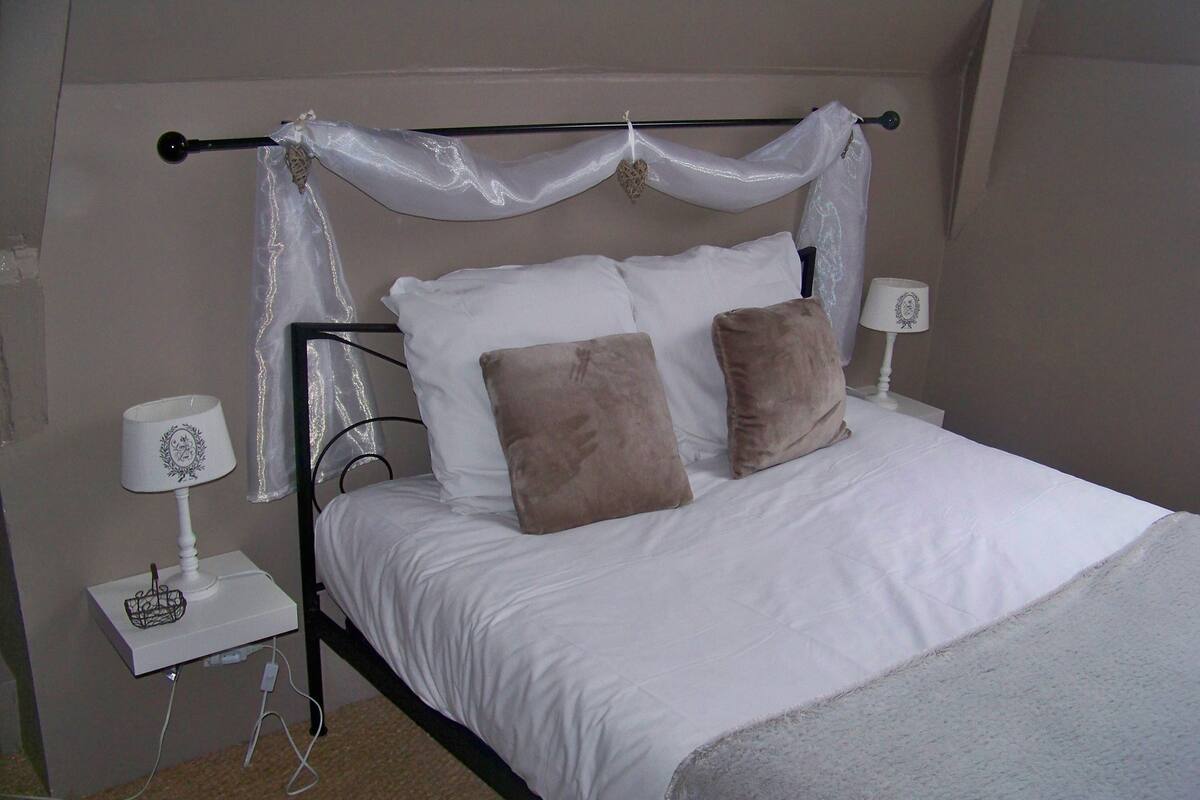 A neatly made bed with white bedding and two brown pillows, a bedside table with a lamp, and a power cord on the floor.