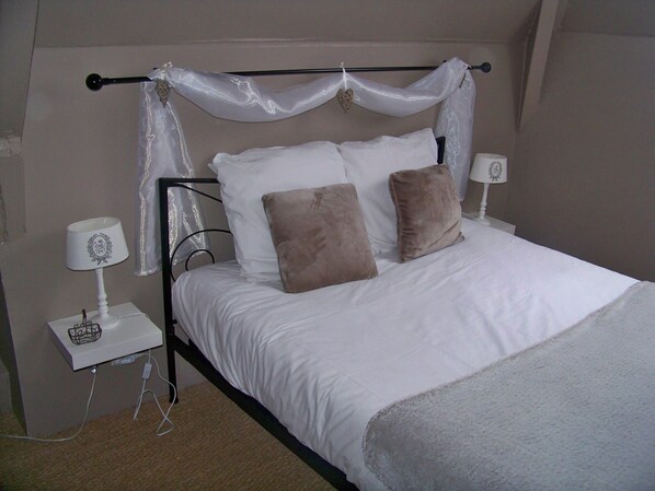 Una cama bien hecha con ropa blanca y dos almohadas marrones, una mesita de noche con una lámpara y un cable de corriente en el suelo.