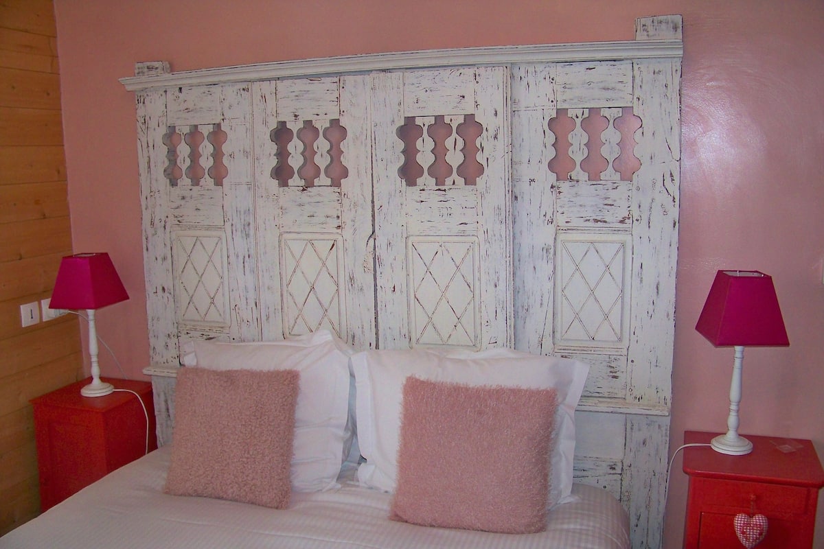 A bedroom with a white bed, pink pillows, and two red nightstands with lamps.
