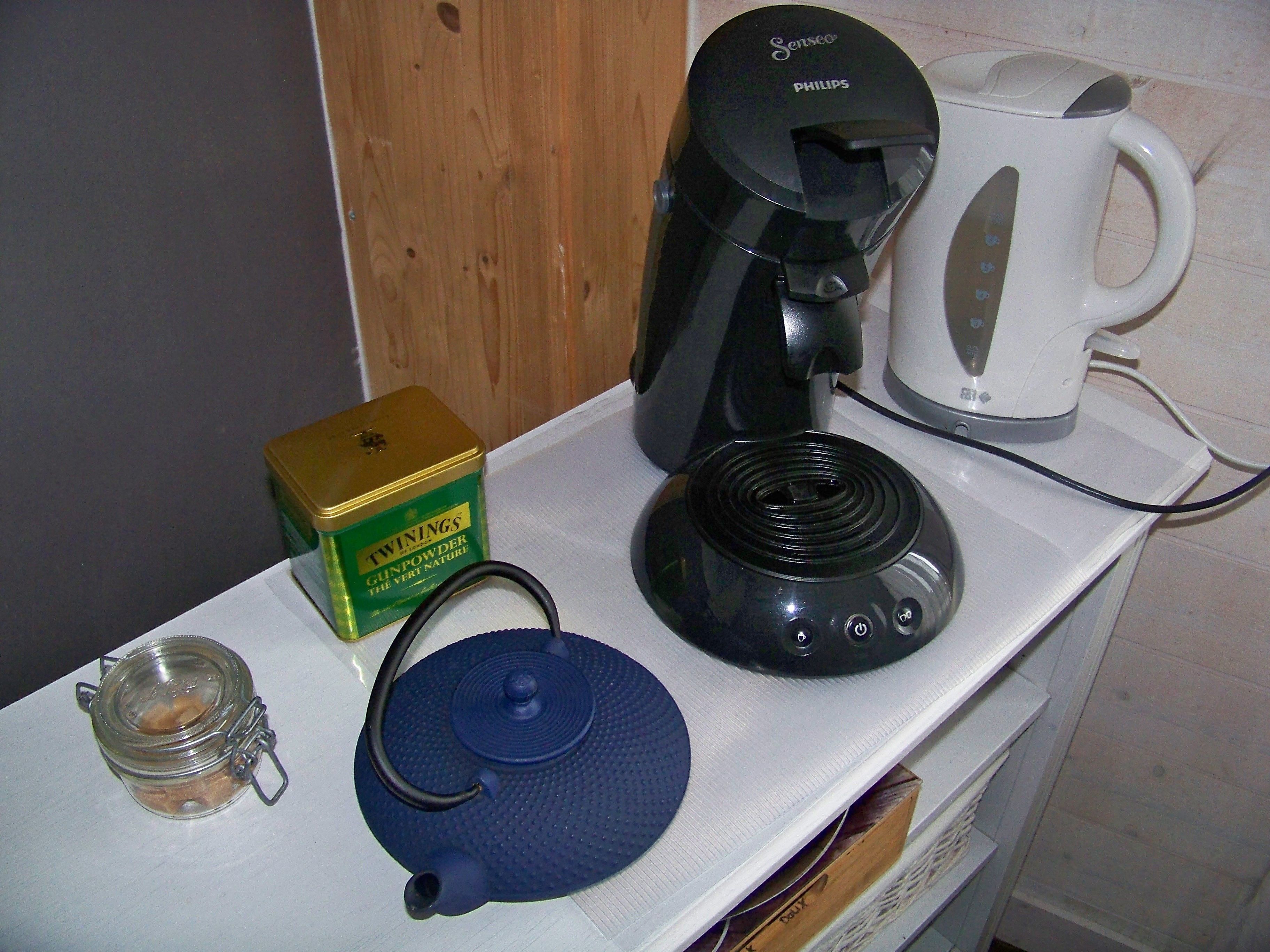 A kitchen counter with a coffee maker, a teapot, a box of Twinings Gunpowder tea, and a kettle.