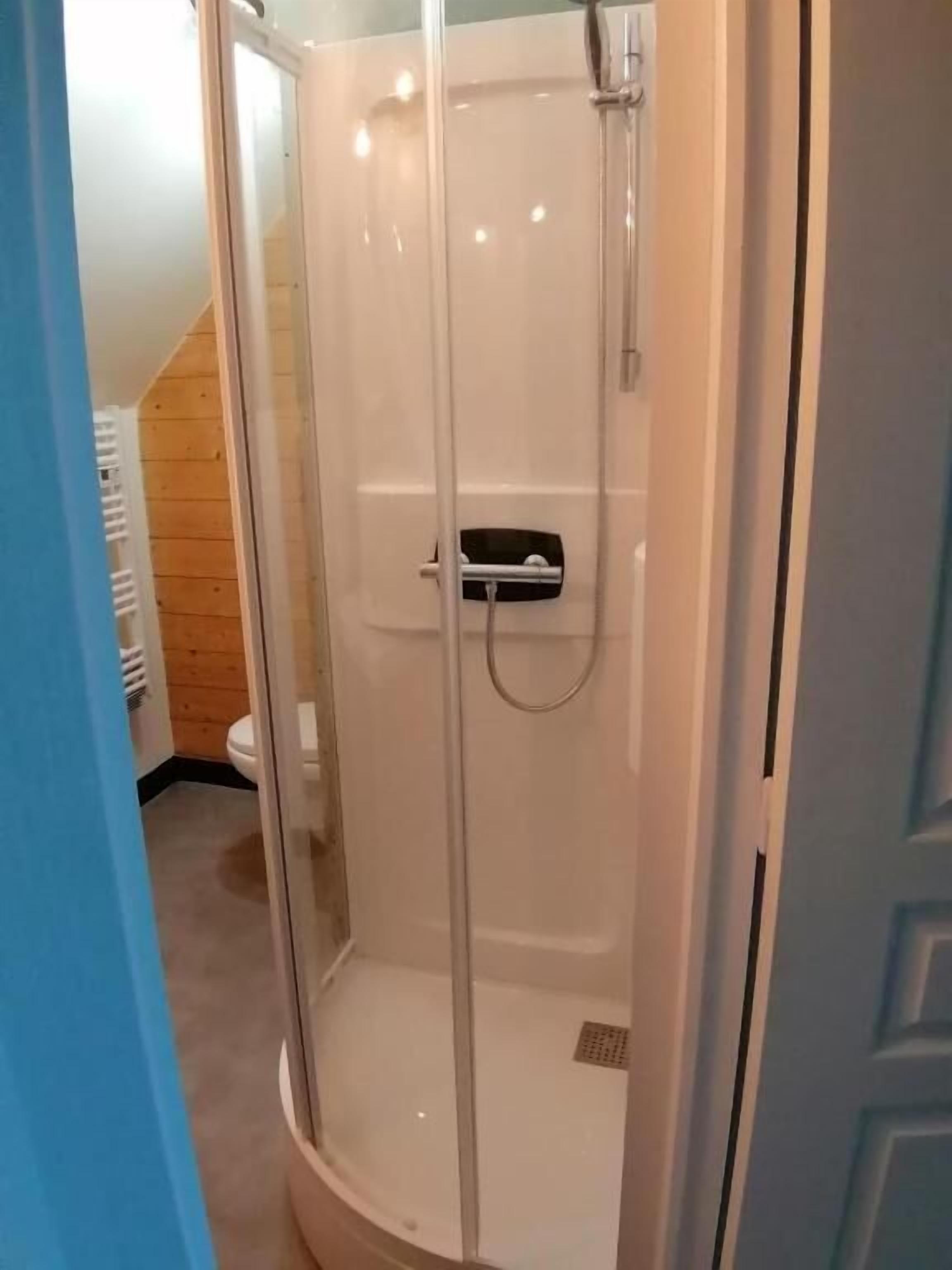 A glass-enclosed shower stall with a handheld showerhead and a control panel.