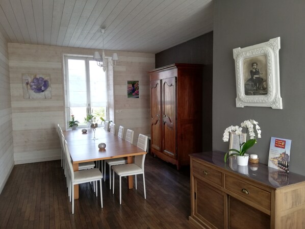 Un comedor con una mesa de madera y sillas blancas, un aparador de madera y un cuadro en la pared.