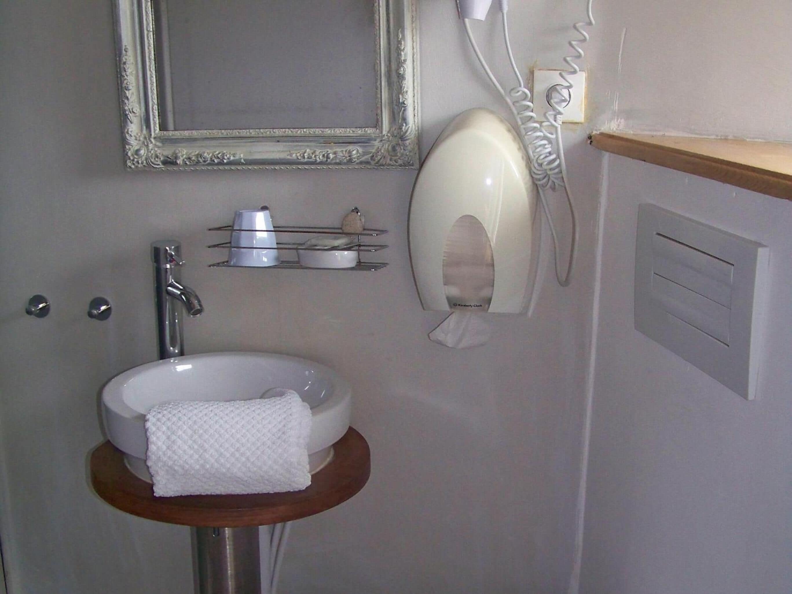Une salle de bain équipée d’un lavabo, d’un miroir, d’un distributeur de serviettes et d’une étagère contenant des articles de toilette.