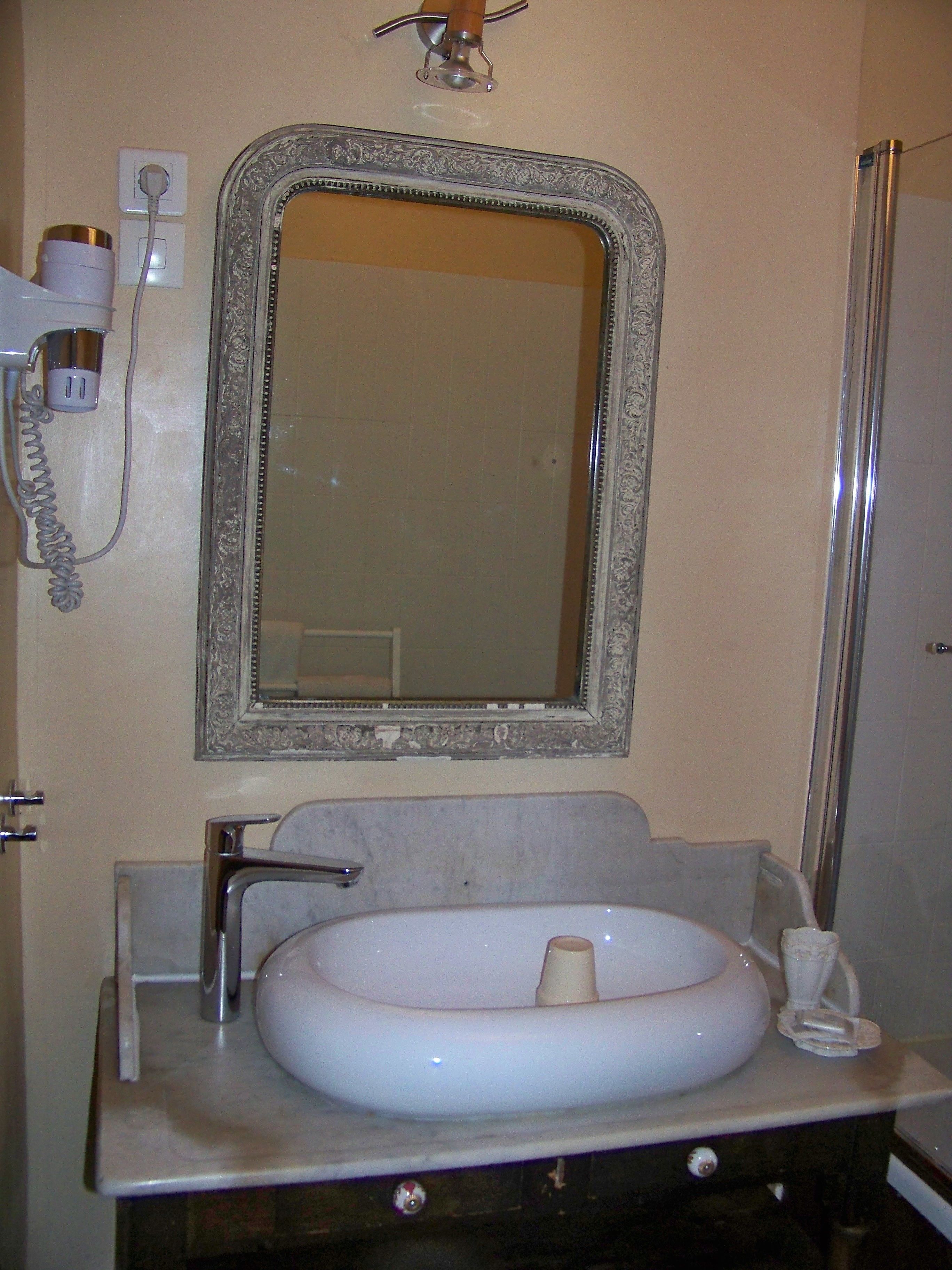 A bathroom with a white sink, a mirror with an ornate frame, and a towel rack.