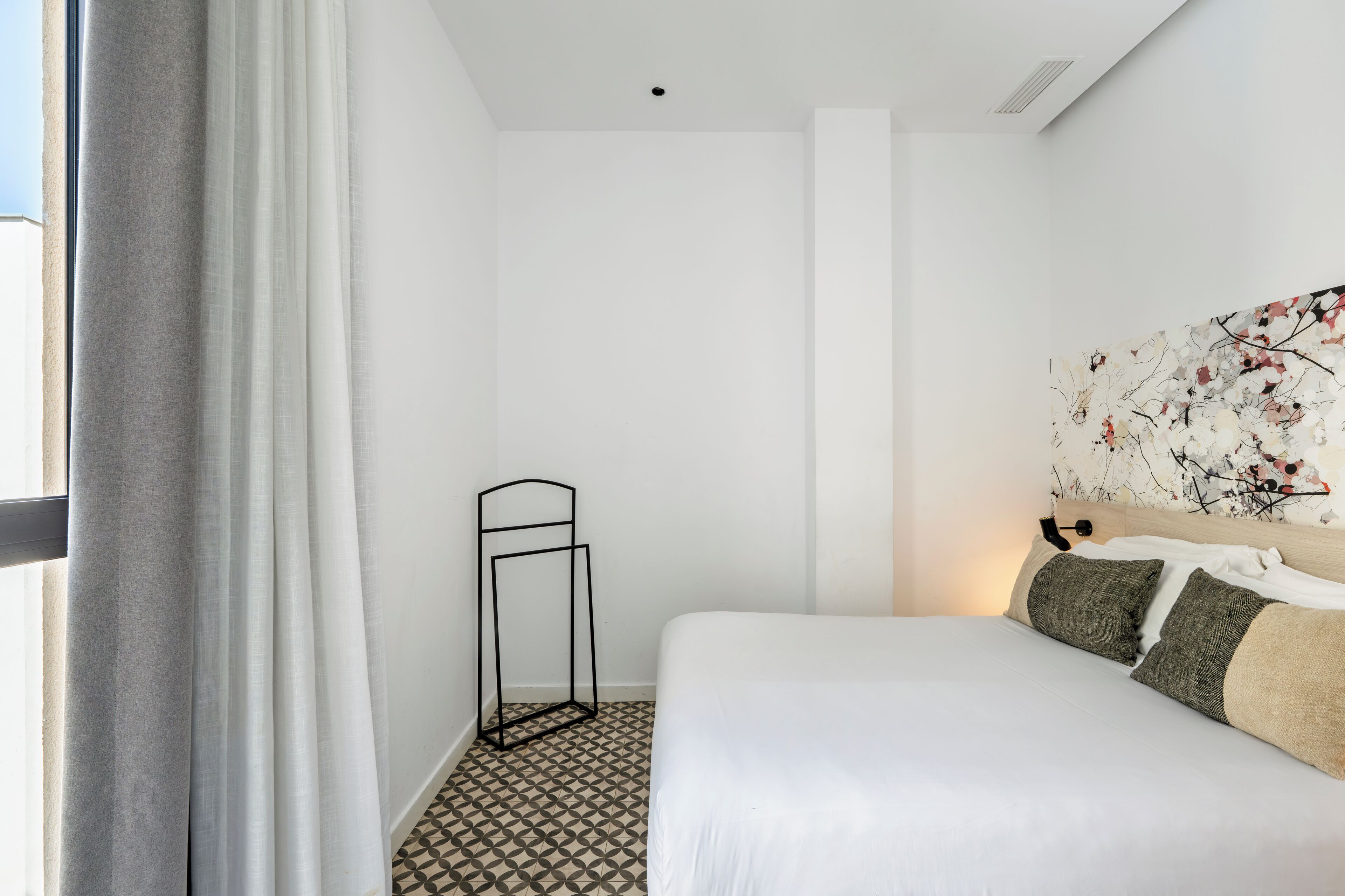 A hotel room with a bed, a standing lamp, a wall art piece, and a patterned floor.