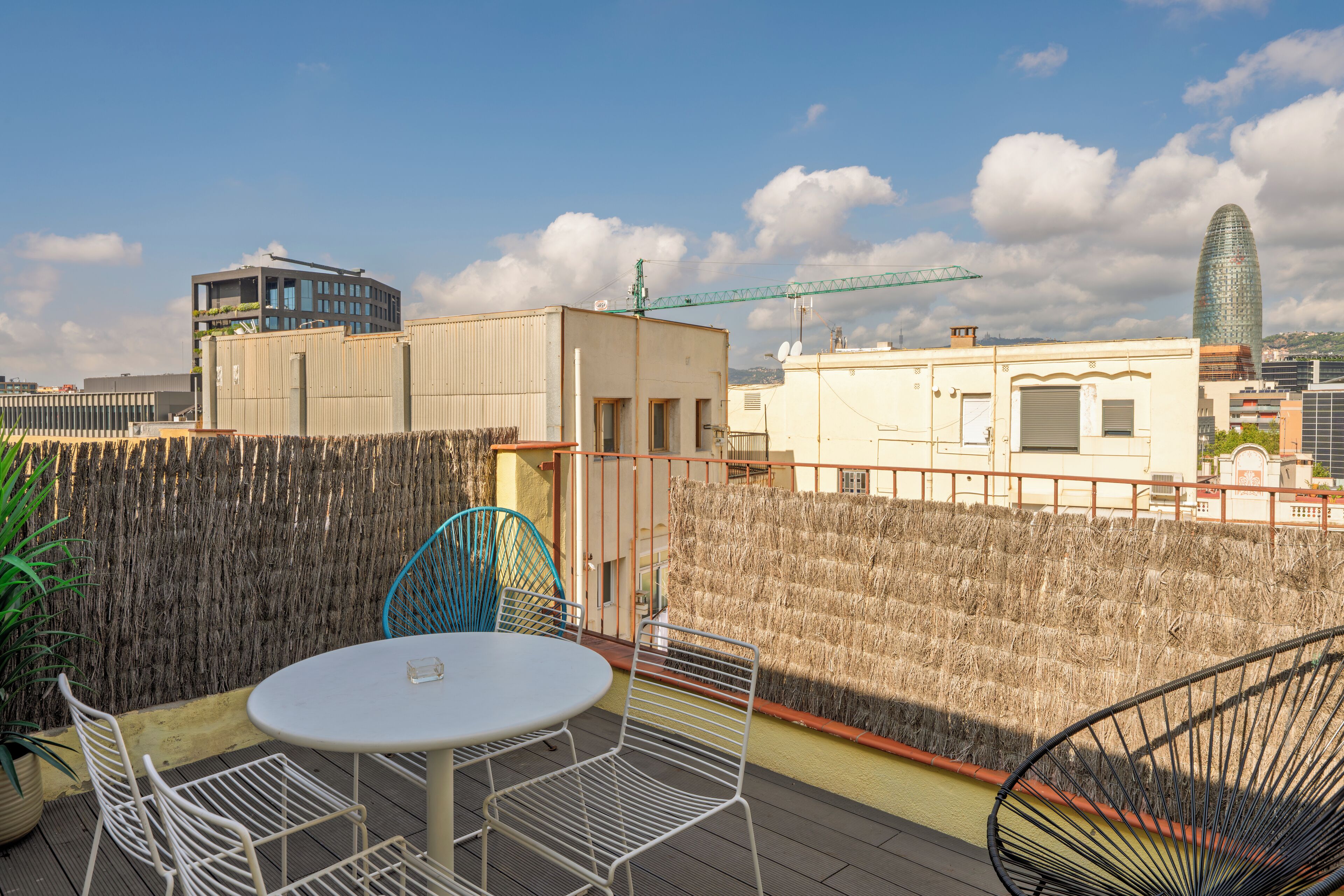 Eine Dachterrasse mit rundem Tisch und Stühlen, Blick auf die Stadtlandschaft und ein Baukran im Hintergrund.