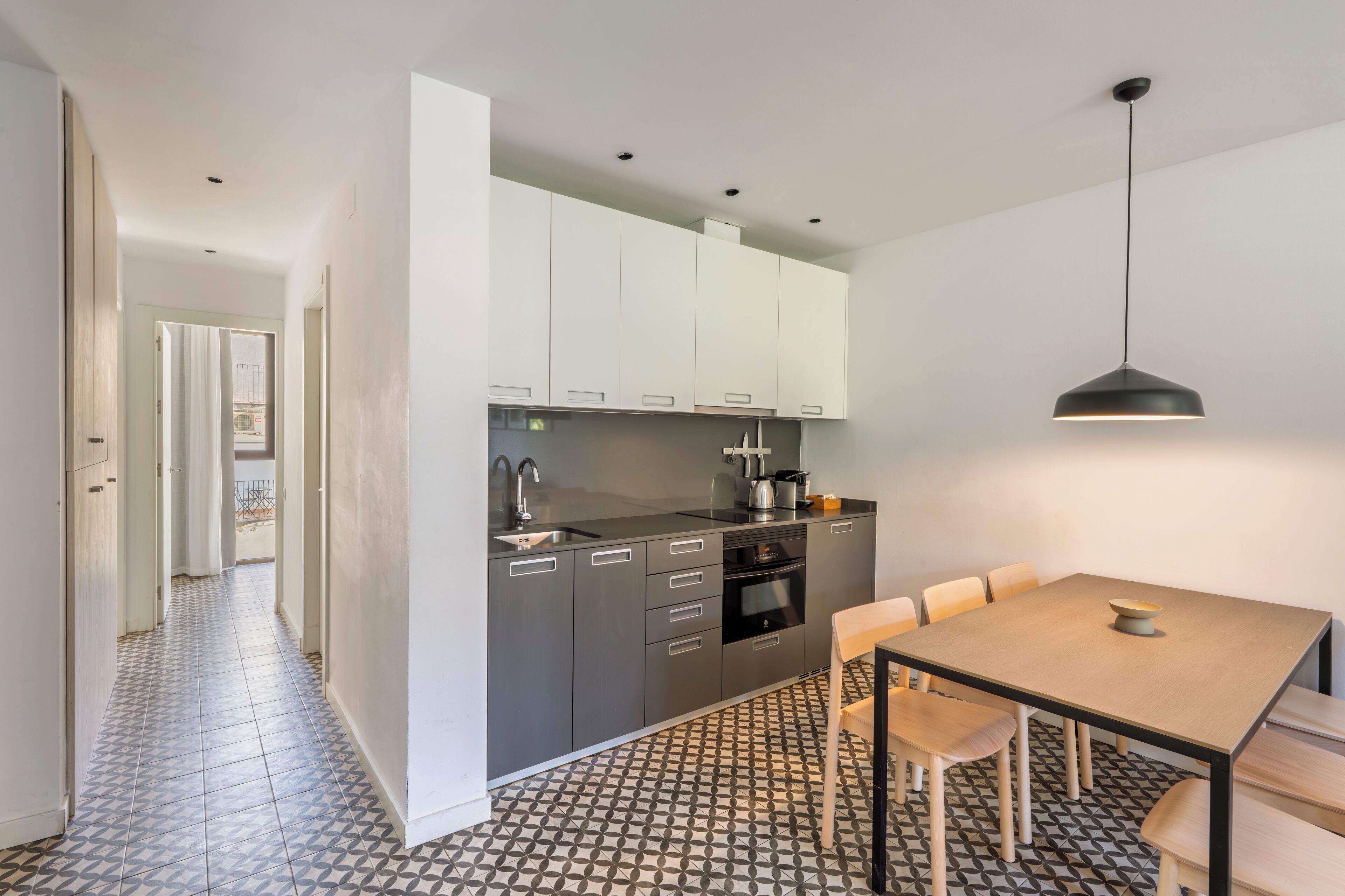 Une cuisine moderne avec des meubles gris, un plan de travail noir et un coin repas comprenant une table et des chaises en bois.