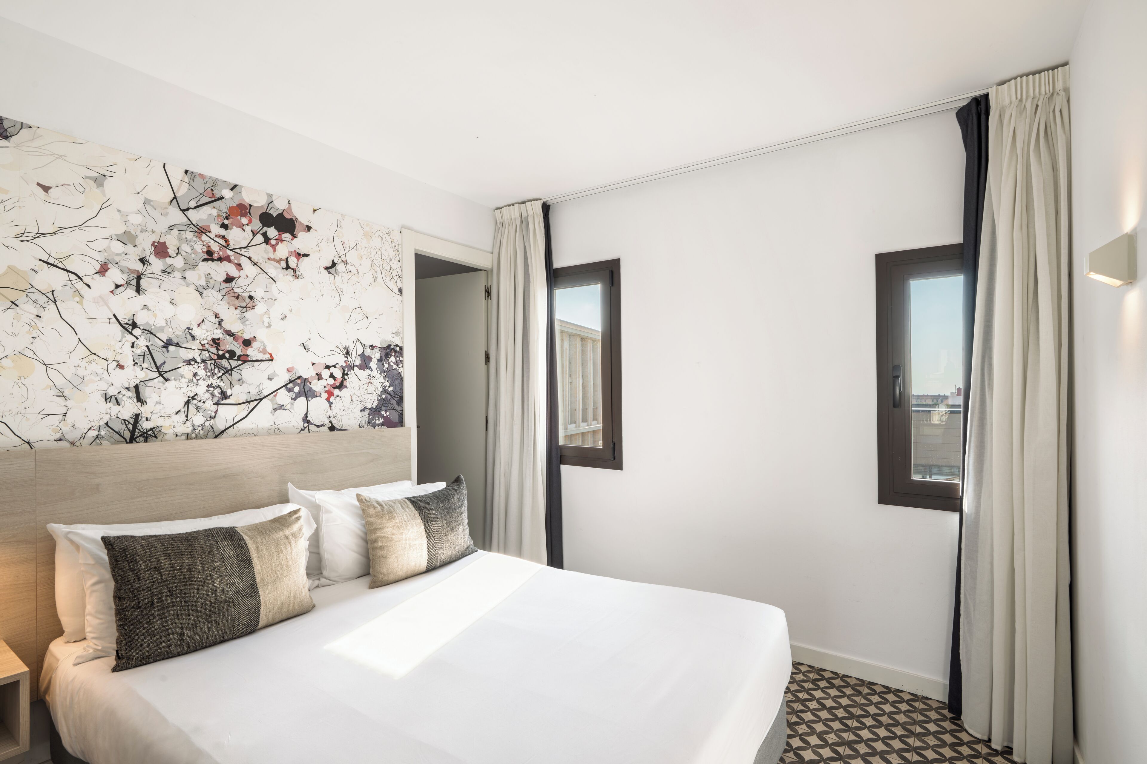 Ein Hotelzimmer mit einem großen Bett, einem modernen Kopfteil, einem großen abstrakten Gemälde und einem Fenster mit Vorhängen.