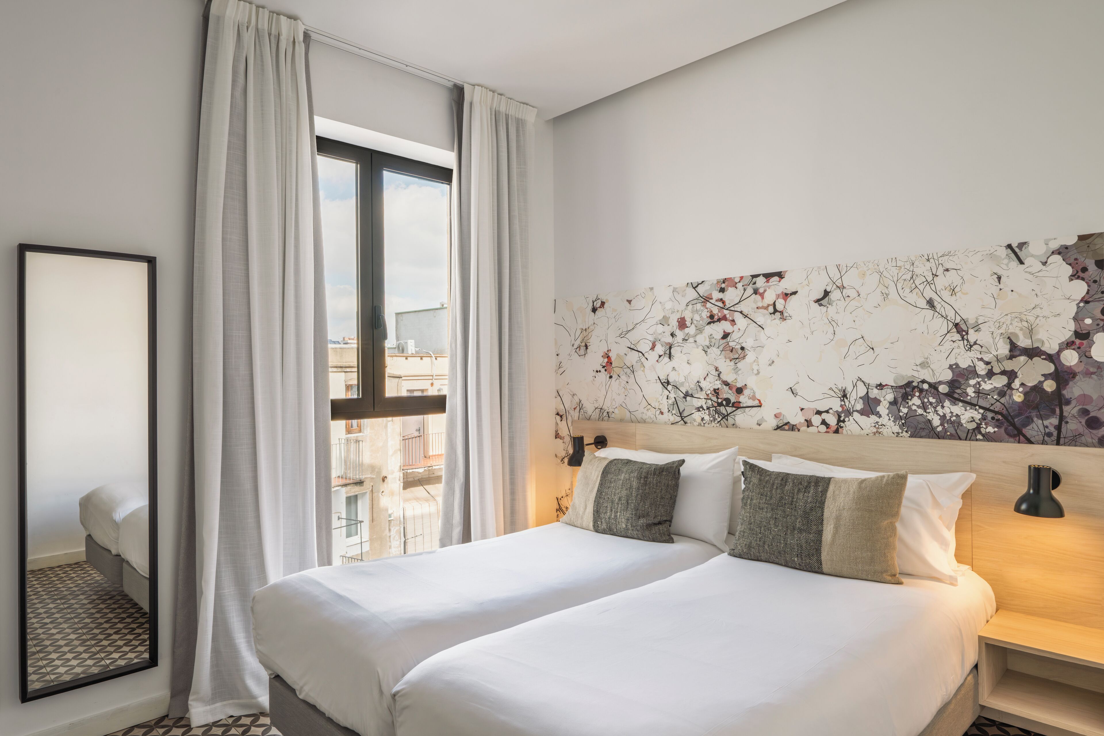 Een hotelkamer met een groot bed, een nachtkastje, een wandlamp en een raam met gordijnen.