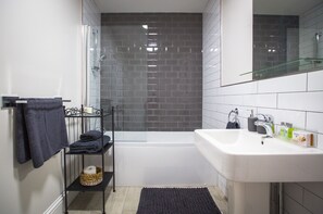 A modern bathroom with a glass shower enclosure, a white bathtub, and a sink with toiletries. - Bay Tree Apartments (Derby)