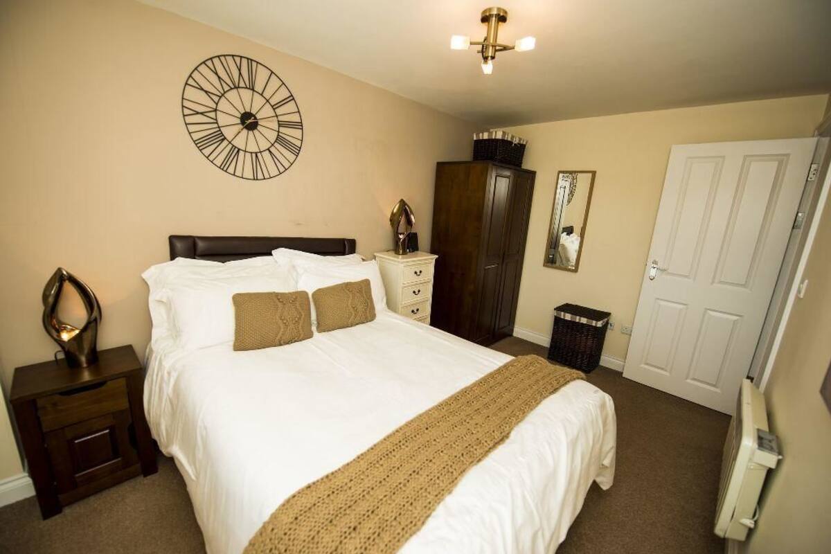 Quarto com uma cama grande, um relógio na parede, cômoda, guarda-roupa e uma porta.