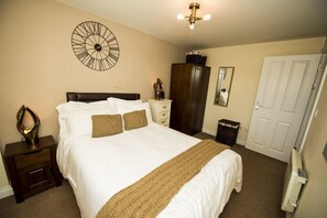 A bedroom with a large bed, a clock on the wall, a dresser, a wardrobe, and a door. - Bay Tree Apartments (Derby)