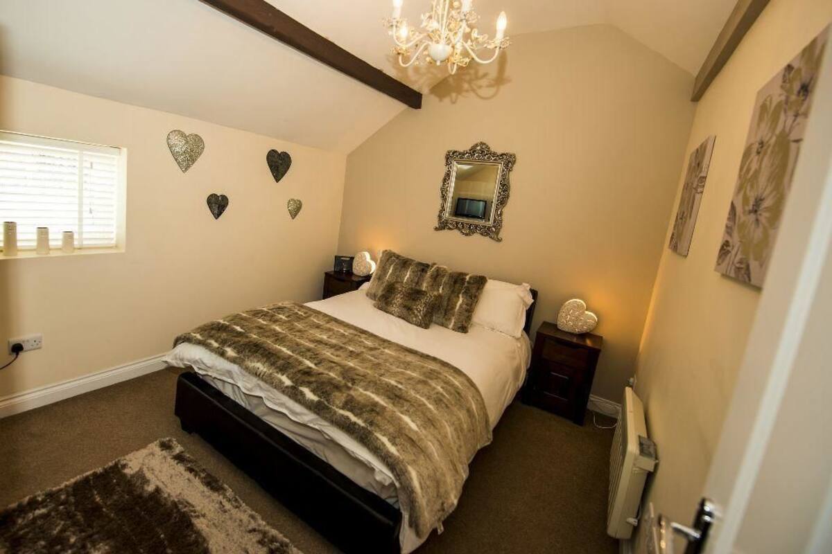 Quarto com cama, lustre, decorações em formato de coração, espelho e radiador.