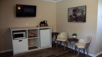 A compact living space with a kitchenette, a television, a painting, and seating.