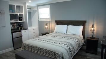 Ein Schlafzimmer mit Bett, Nachttischen, einer Bank, einer integrierten Küchenzeile und einem Fenster.