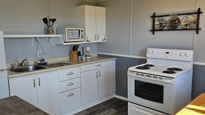 A compact kitchen with white cabinets, a microwave, a stove, and a ceiling fan. - Carleton Inn and Cottages (Carleton Corner)