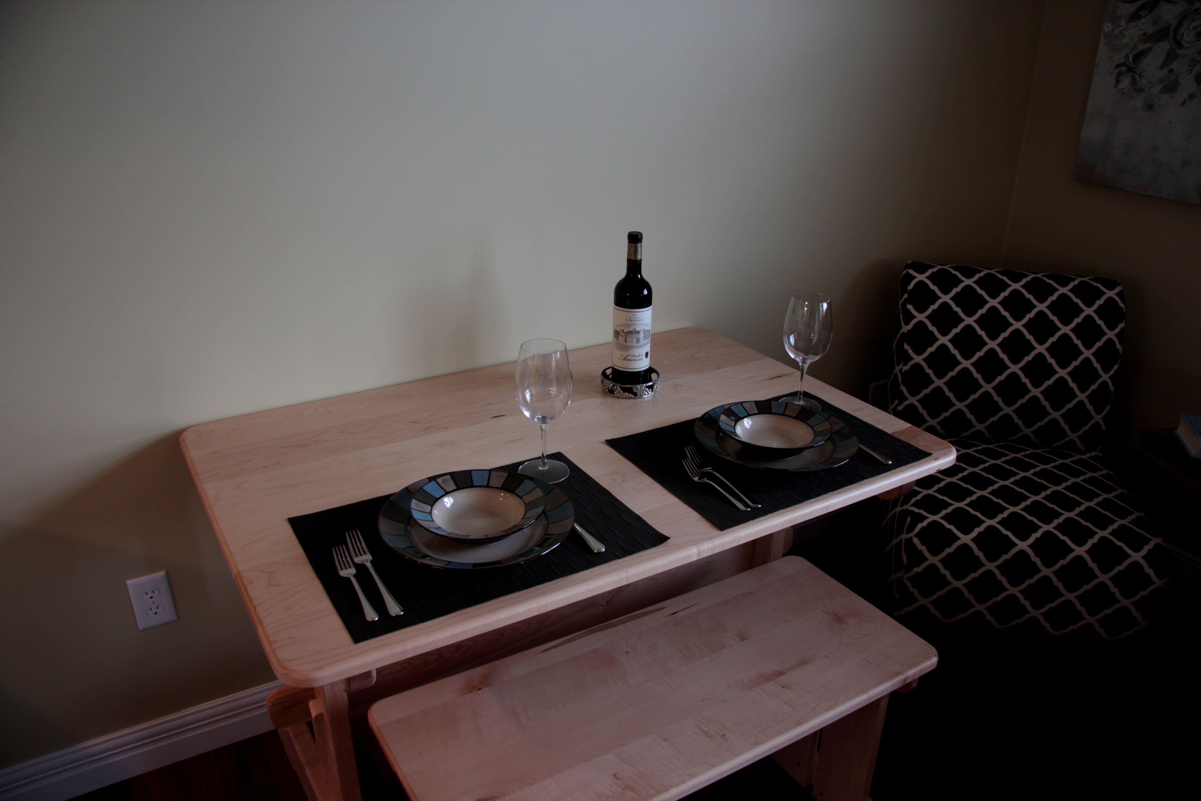 A dining table with two plates, a wine bottle, and cutlery.