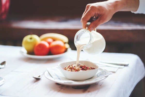 Desayuno con un tazón de cereal, una fuente de frutas y una mano sirviendo leche.