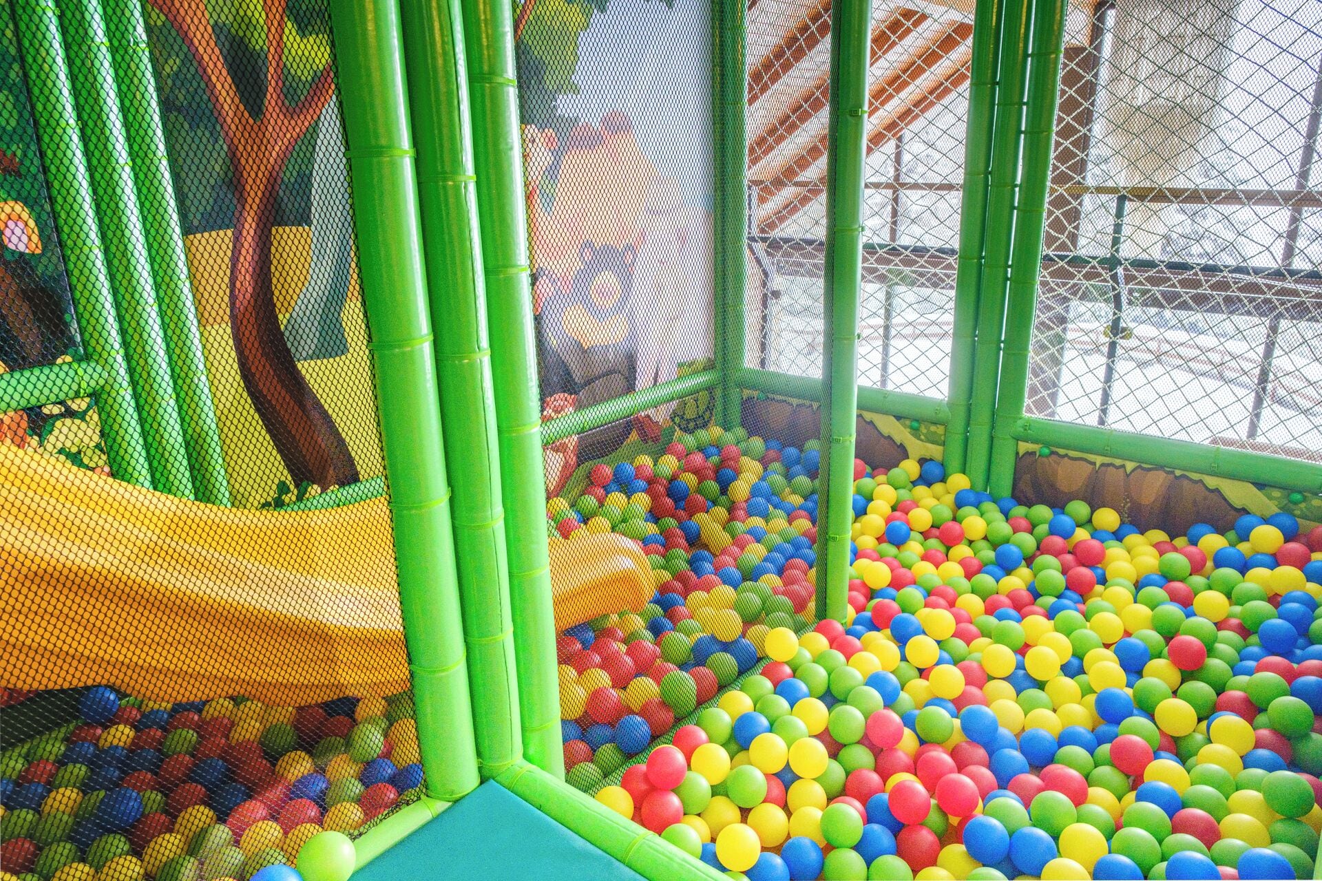 A children's play area with a netted enclosure, colorful plastic balls, and a slide.