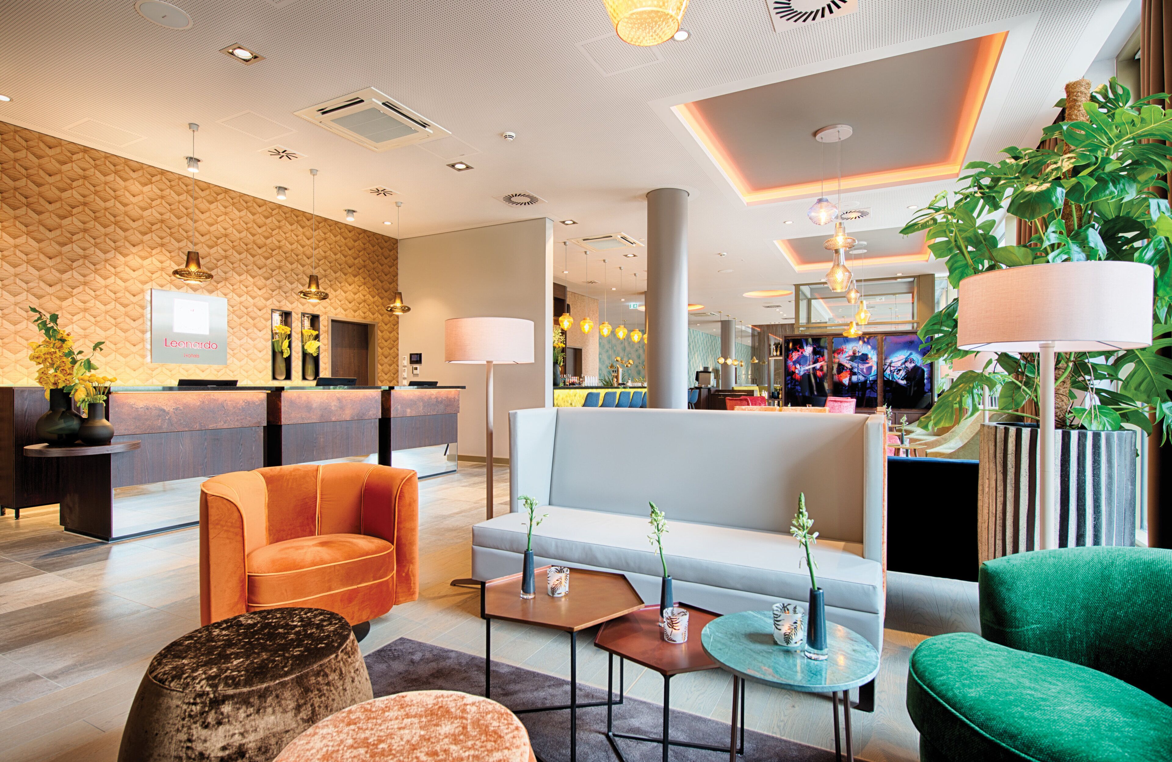 A hotel lobby with a reception desk, seating area, and a television screen displaying a band.