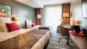 A hotel room with two beds, a desk, a chair, and a television. - Leonardo Royal Hotel Ulm (Ulm)