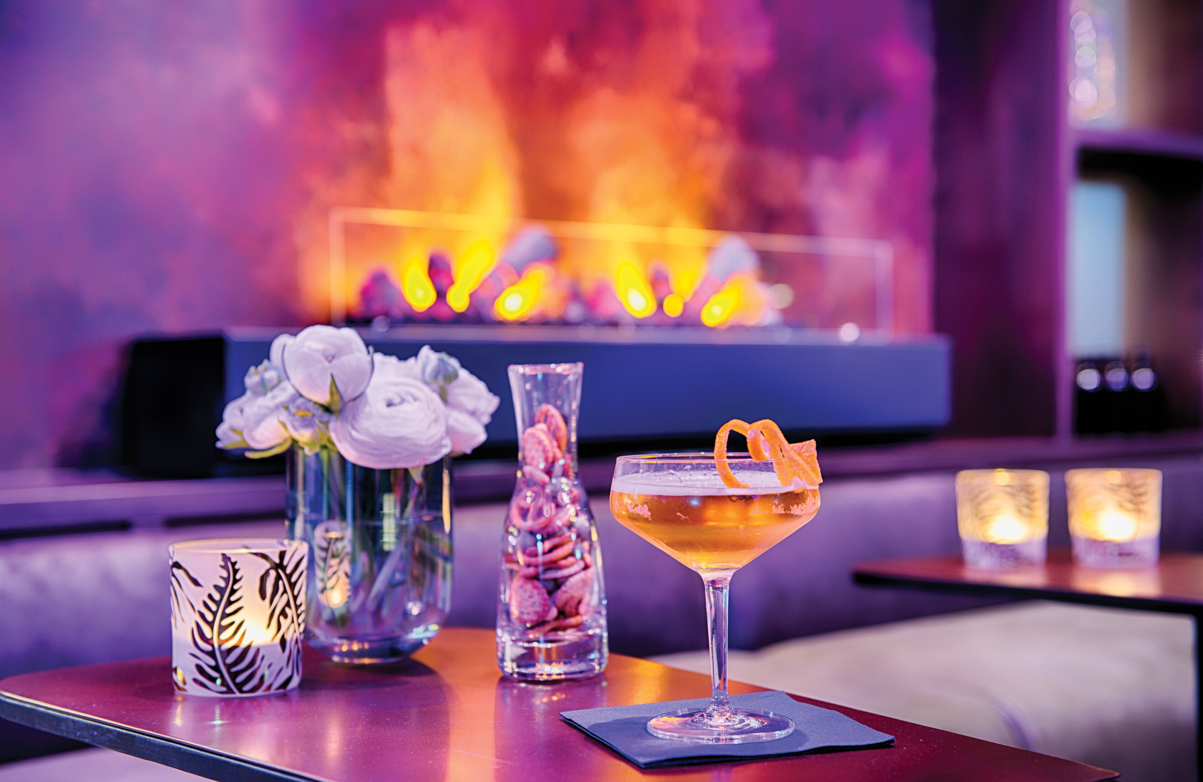 A bar area with a cocktail, a vase with flowers, and a decorative candle.