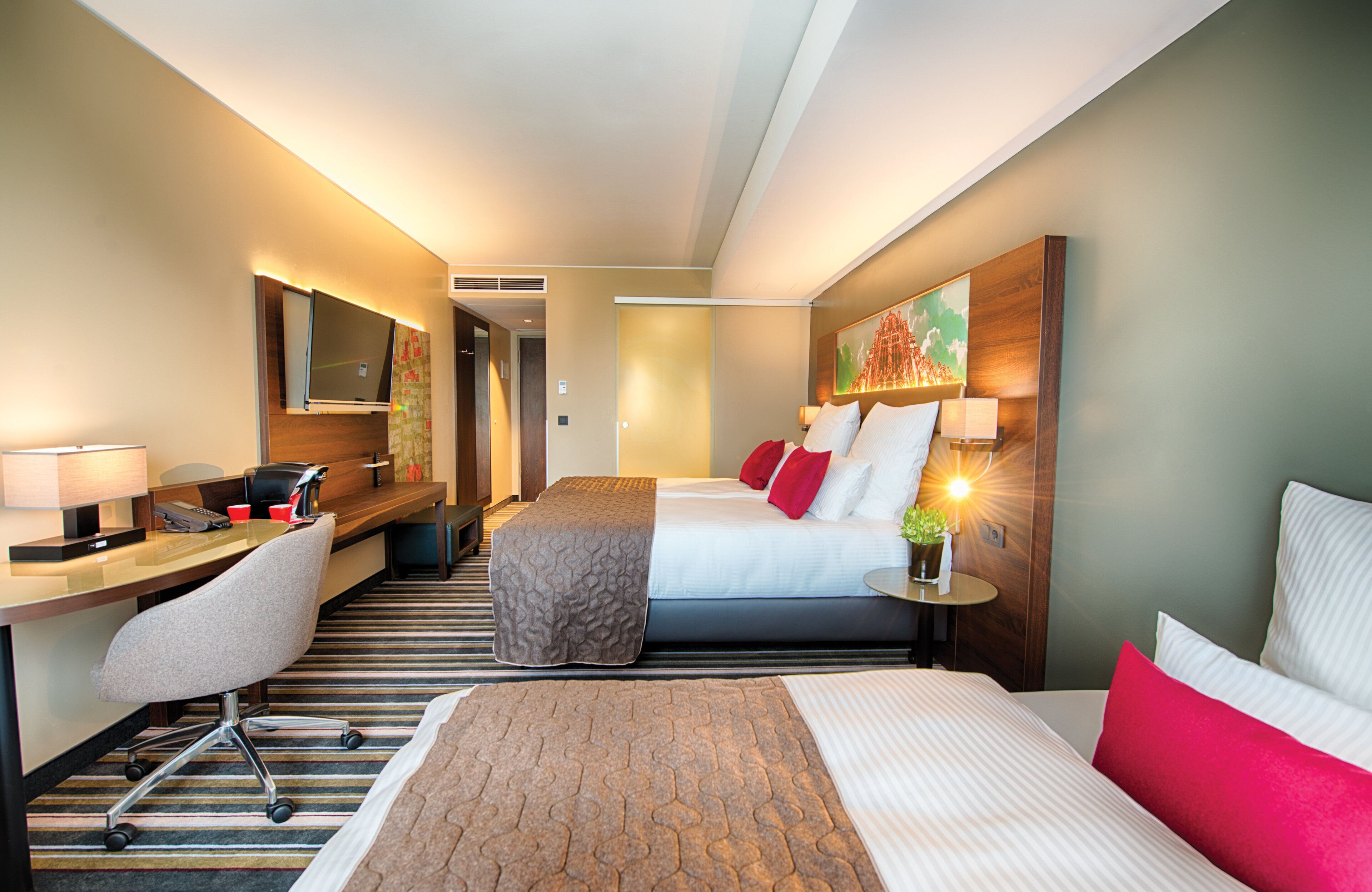 Habitación de hotel con cama, escritorio, silla y un cuadro grande en la pared.