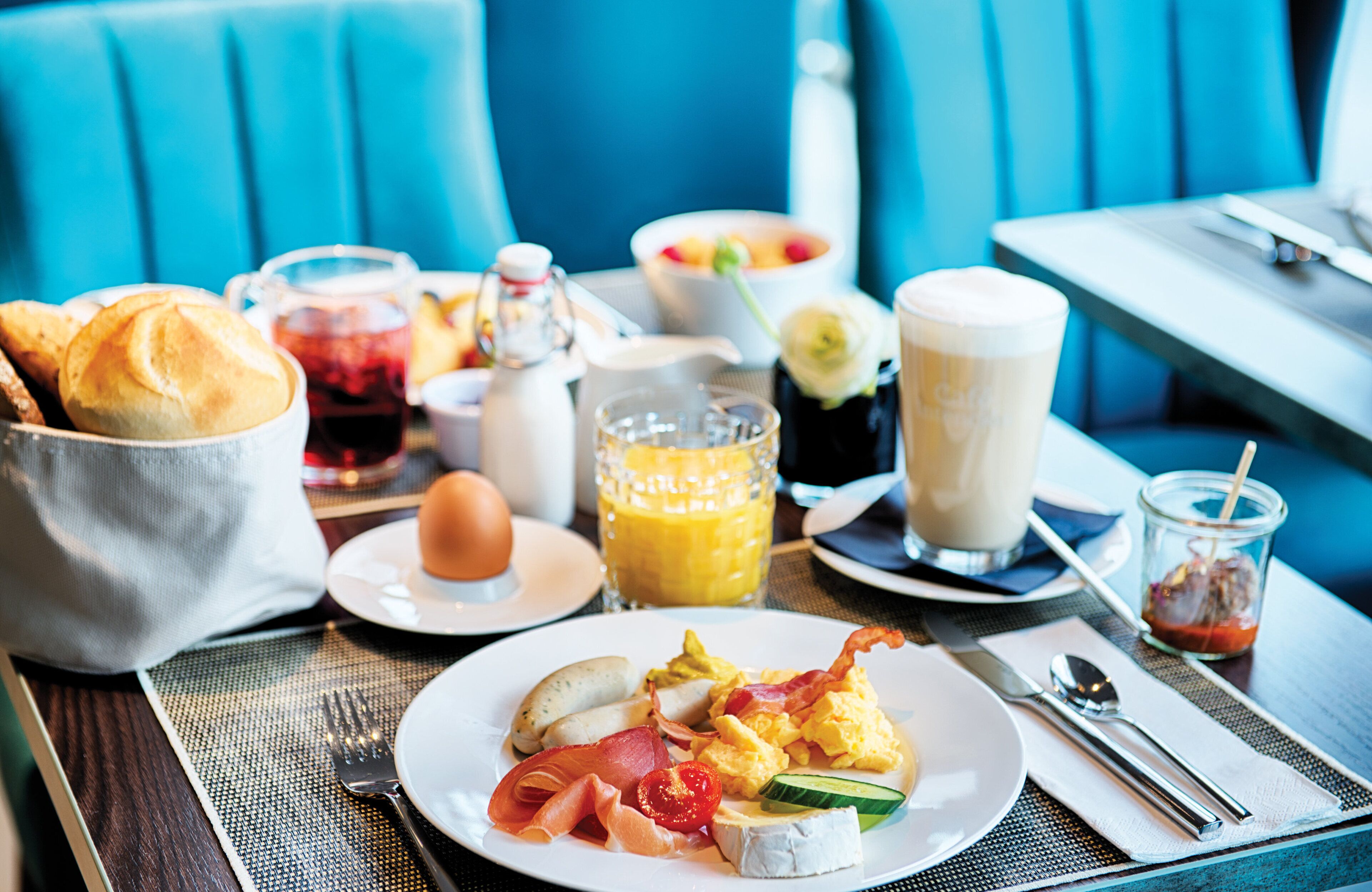 A breakfast setting with a plate of eggs, bacon, cheese, and vegetables, a glass of orange juice, a cup of coffee, and a pitcher of tea.