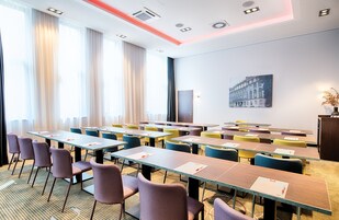 Un salón de conferencias con varias mesas y sillas, un amplio ventanal con cortinas, y un cuadro en la pared.