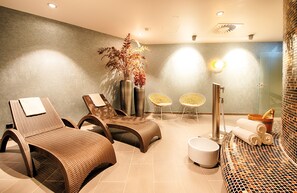 A spa area with two wicker lounge chairs, a small table, a tall vase with dried plants, a wall-mounted light, and a tiled floor. - Leonardo Royal Hotel Ulm (Ulm)